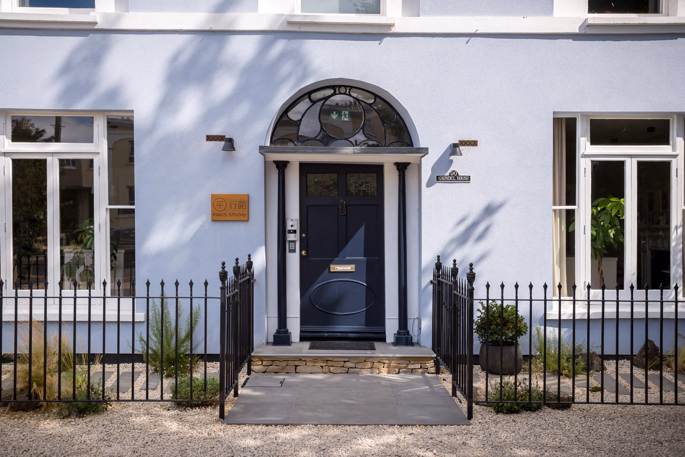 Blue arched doorway with black door, flanked by windows and black metal fence with plants around.