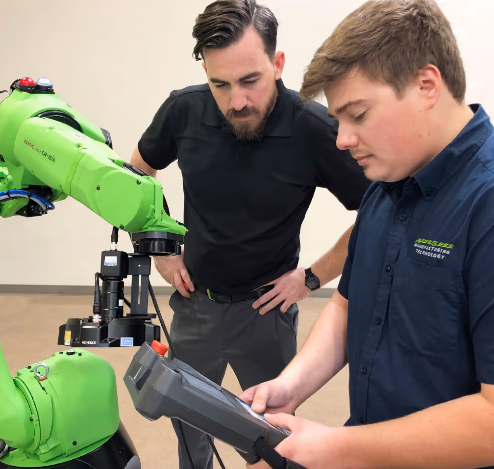 An AeroSpec associate operates a handheld controller to program a robotic arm for testing, with another associate standing nearby and watching the procedure closely.