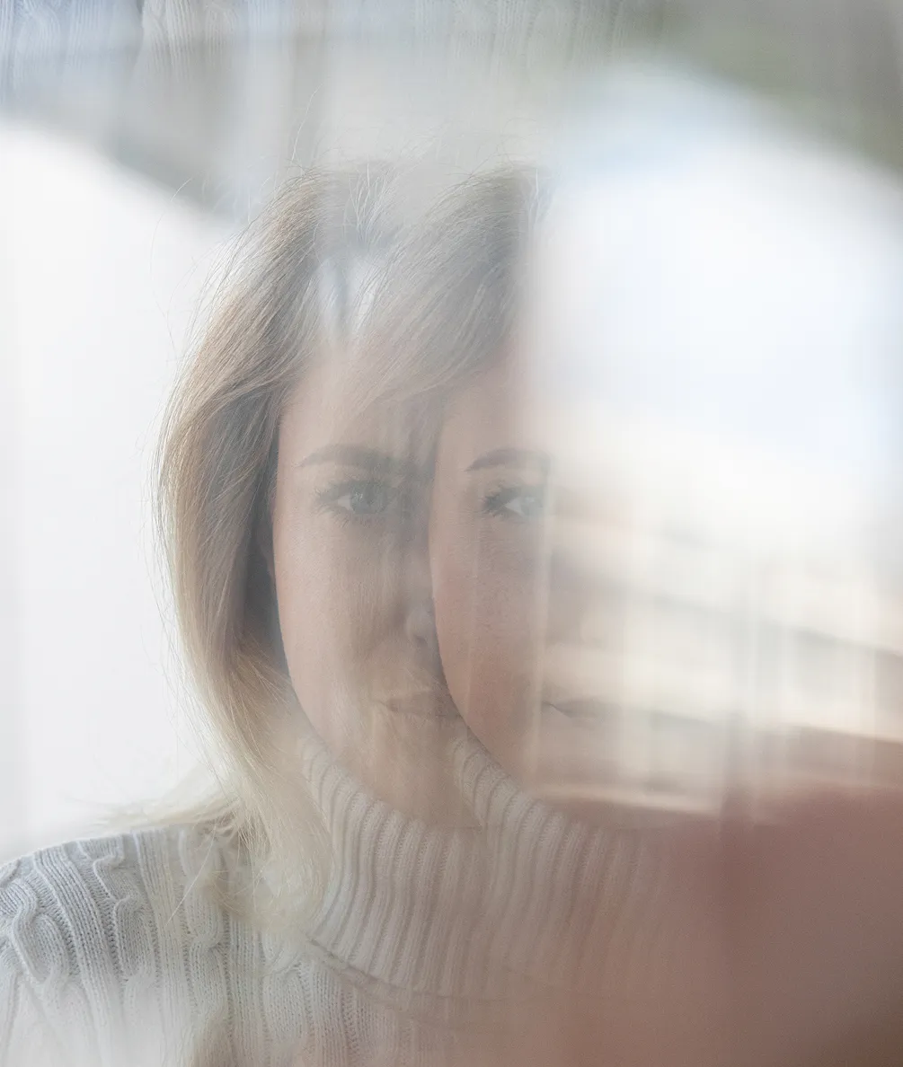 Blurry image of a woman wearing a white knitted turtleneck sweater, with a double-exposure effect creating two overlapping faces.