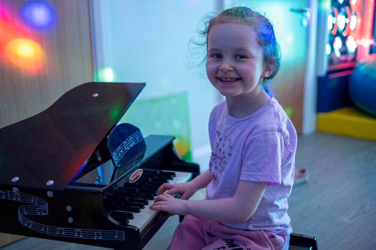 A smiling girl playing the piano at Rebecca House