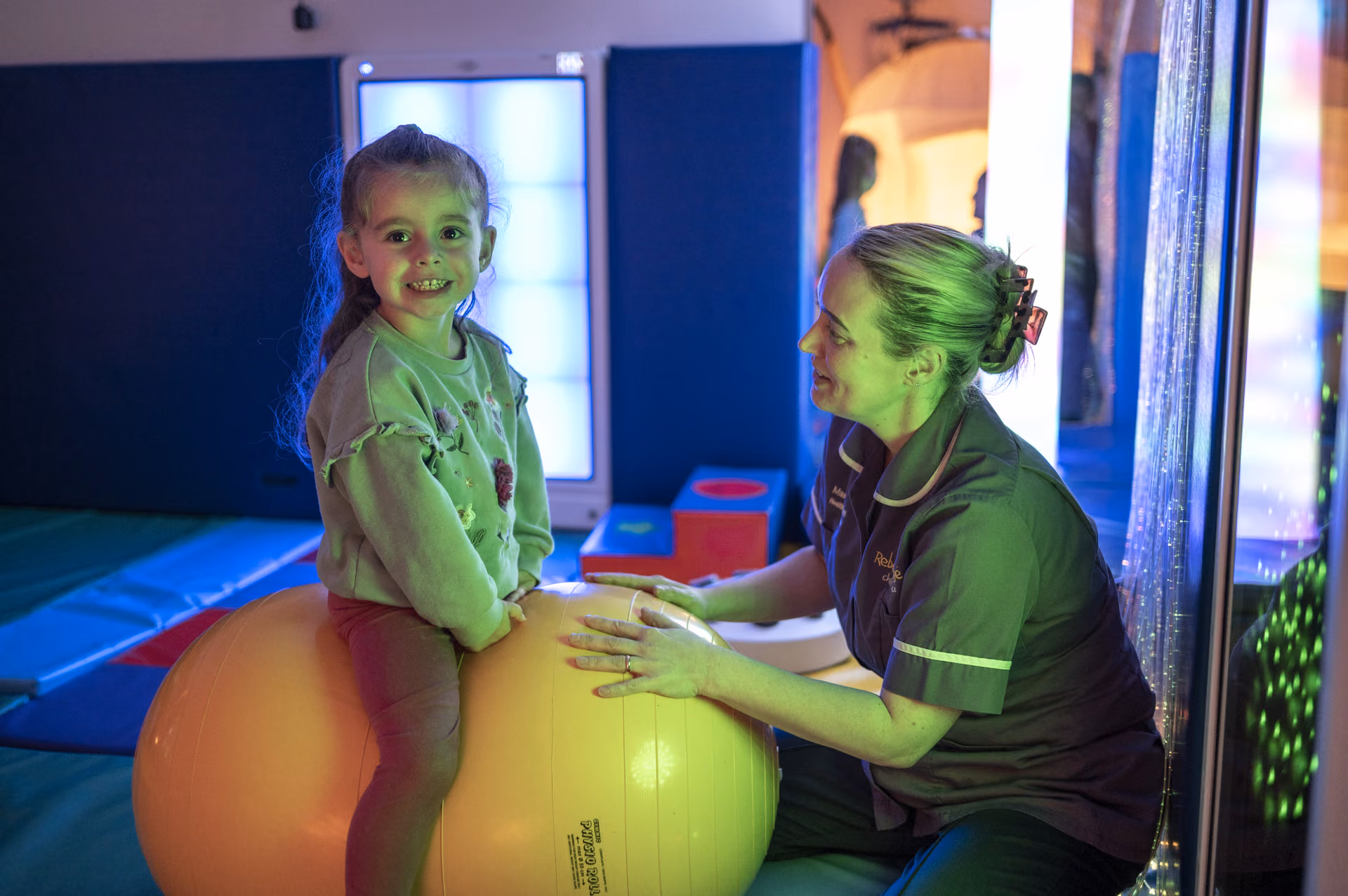 A Rebecca House carer and a smiling girl in the sensory room