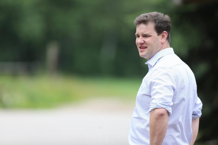 Mann im hellblauen Hemd steht im Freien und schaut nach rechts, unscharfer grüner Hintergrund.