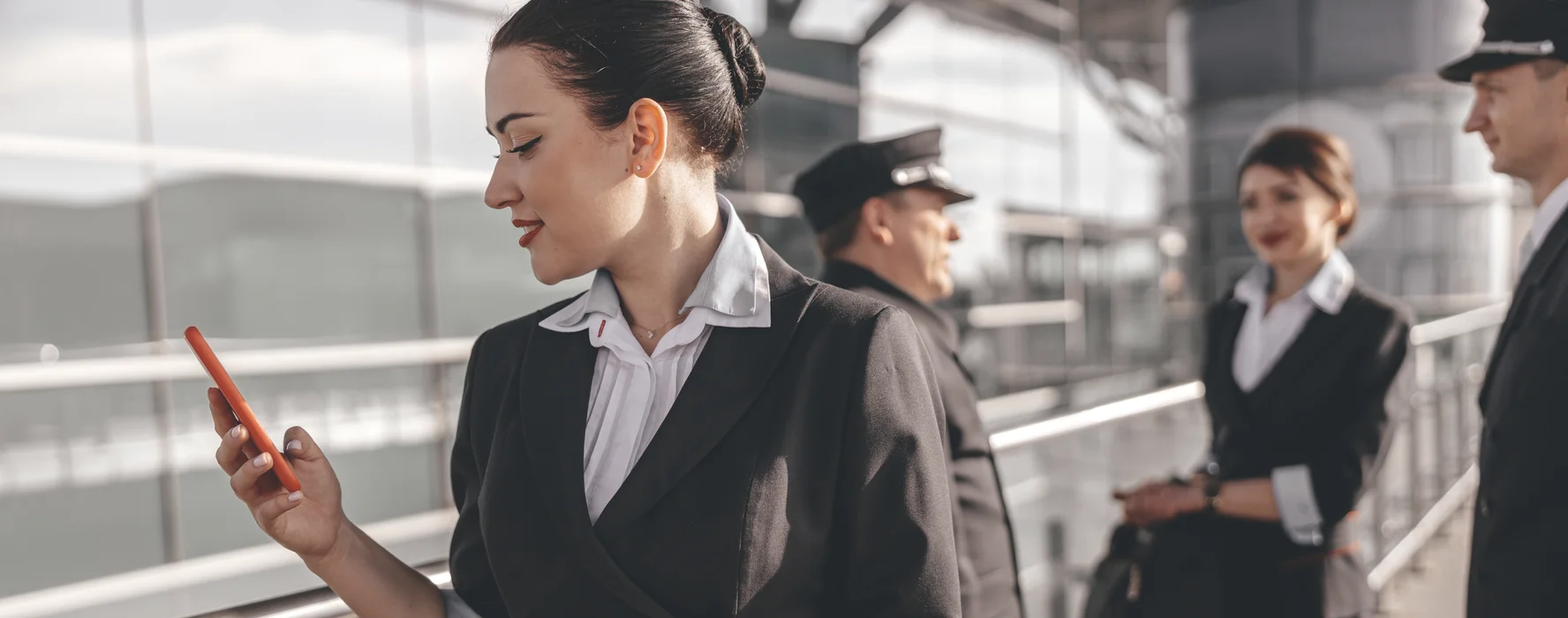 Cabin crew member checking her phone in the terminal with pilots and colleagues