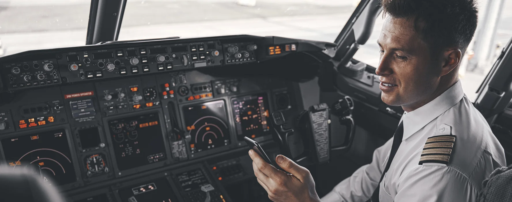 Airline captain in the cockpit checking his roster on a mobile phone