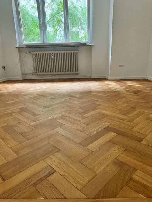 Hellbrauner Fischgrät-Parkettboden von Damian Parkett & Boden in einem renovierten Raum mit viel Tageslicht.
