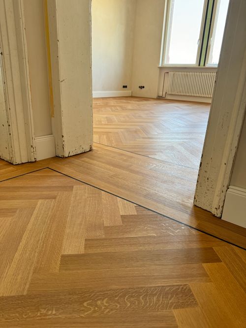 Blick durch eine Türöffnung auf das verlegte Fischgrät-Parkett von Damian Parkett & Boden, das sich im nächsten Raum fortsetzt.