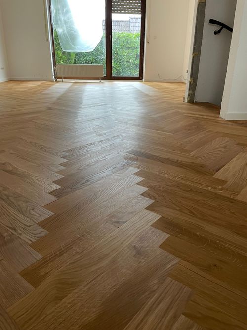 Neu verlegtes Fischgrät-Parkett von Damian Parkett & Boden, das zu einer Balkon- oder Terrassentür führt und den Blick ins Grüne freigibt.