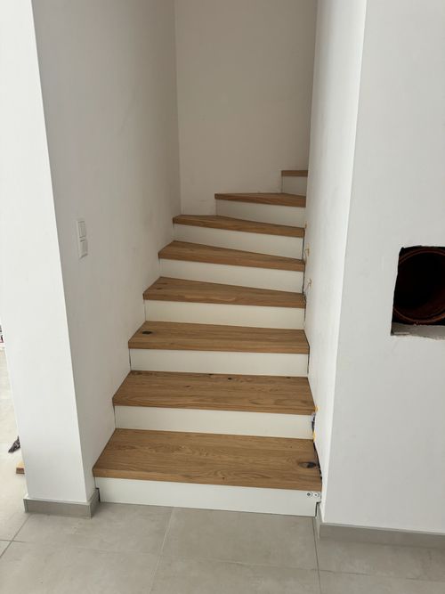 Minimalistische Treppenstufenverkleidung: Helle Holzstufen an weißen Wänden, Referenzprojekt der Treppensanierung durch Damian Parkett & Boden.