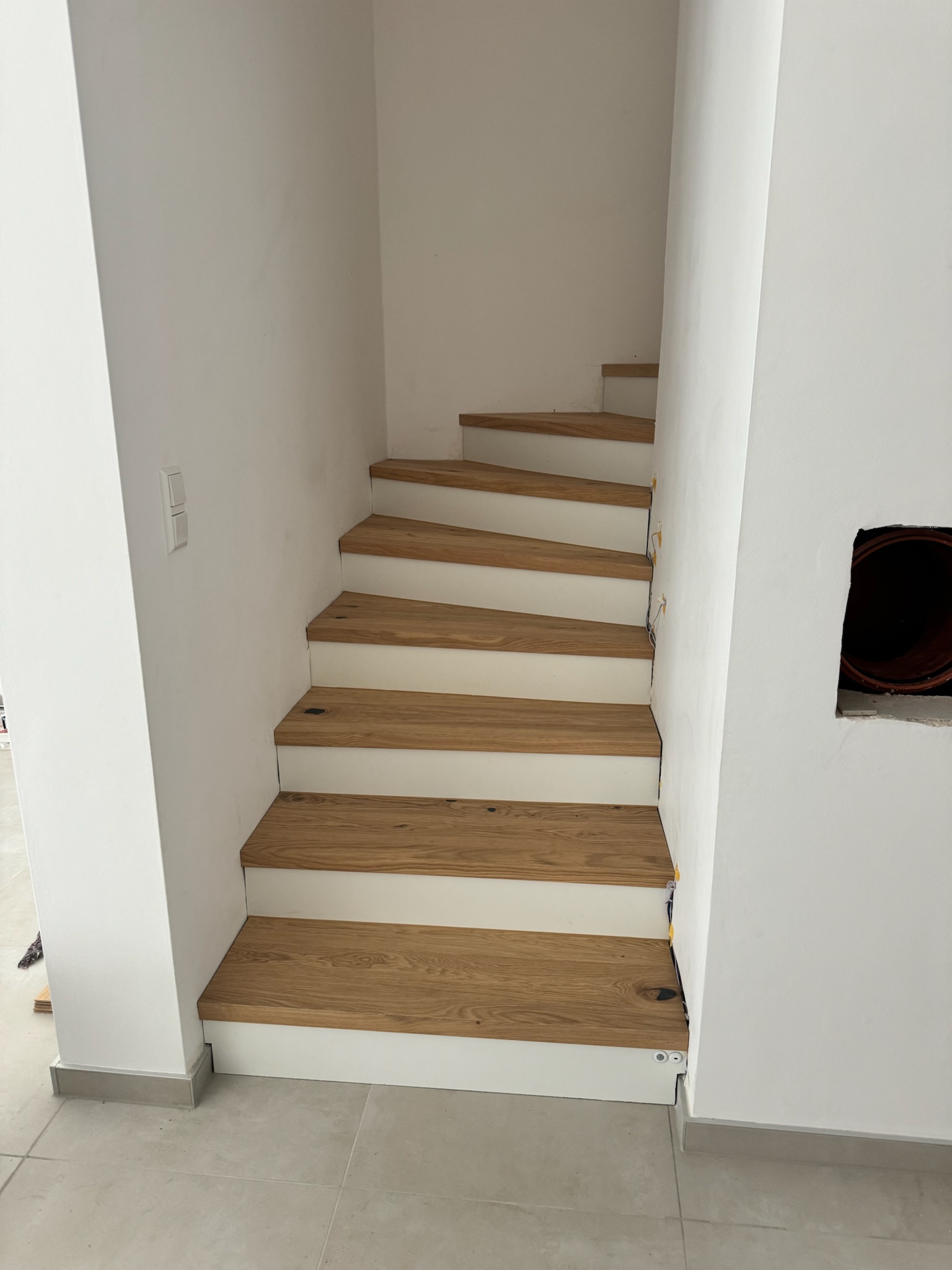 Minimalistische Treppenstufenverkleidung: Helle Holzstufen an weißen Wänden, Referenzprojekt der Treppensanierung durch Damian Parkett & Boden.