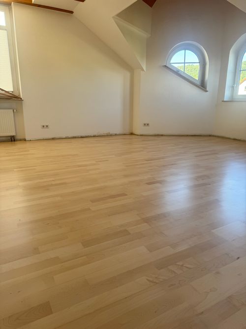 Heller Dachgeschossraum mit schrägen Wänden und Rundfenster, ausgestattet mit hellen Landhausdielen von Damian Parkett & Boden.