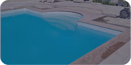 Ein leerer blauer Pool mit runden Eckstufen und einem umgebenden Pflaster.