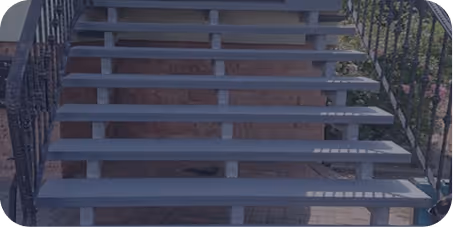 Freitragende Außentreppe aus Metall mit offenen Stufen und schwarzen Geländern auf beiden Seiten.