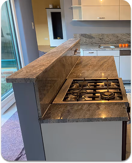 Moderne Küche mit grauer Marmor-Arbeitsplatte und eingebautem Gasherd neben einem Fenster.