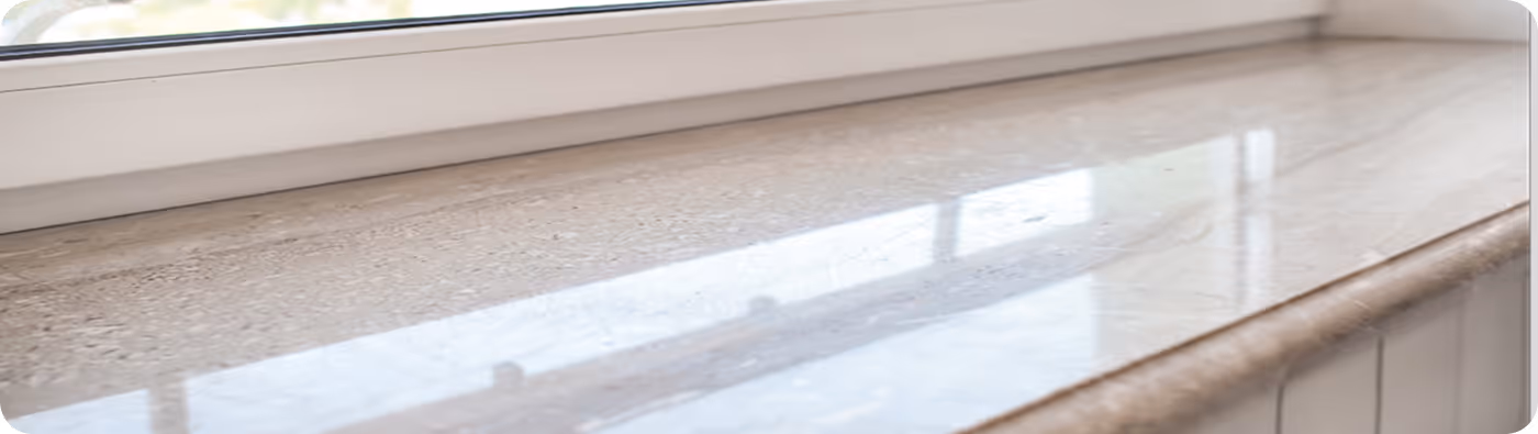 Fensterbank aus hellem, poliertem Marmor mit Spiegelung des Fensters.