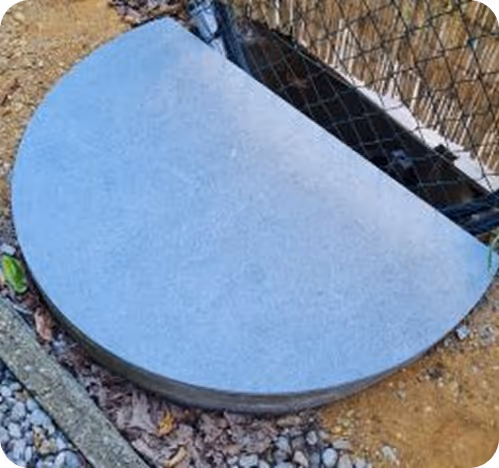 Grauer halbkreisförmiger Steinplatz auf Erde neben einem Drahtzaun und Kieselsteinen.