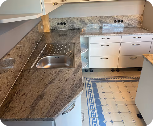 Moderne Küche mit grauem Marmor-Arbeitsplatte, Edelstahlspüle und weißen Schränken auf blau-weiß gekacheltem Boden.