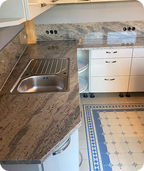 Küchenarbeitsplatte aus grauem Marmor mit integriertem Edelstahlspülbecken und weißer Schubladeneinheit daneben, darüber graue Steckdosenleisten.