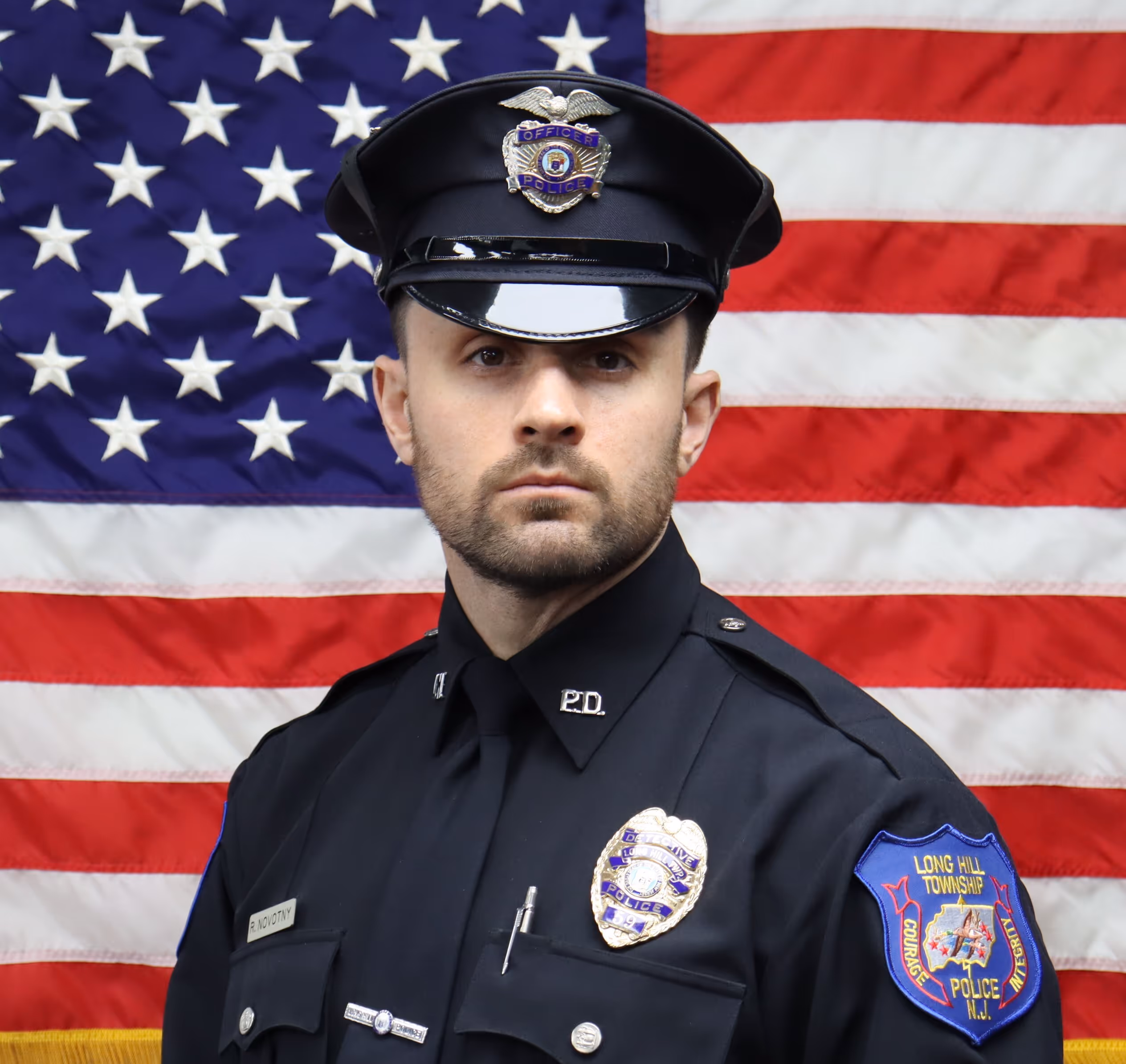 Police officer in uniform with a badge and Long Hill Township Police patch, standing in front of an American flag.