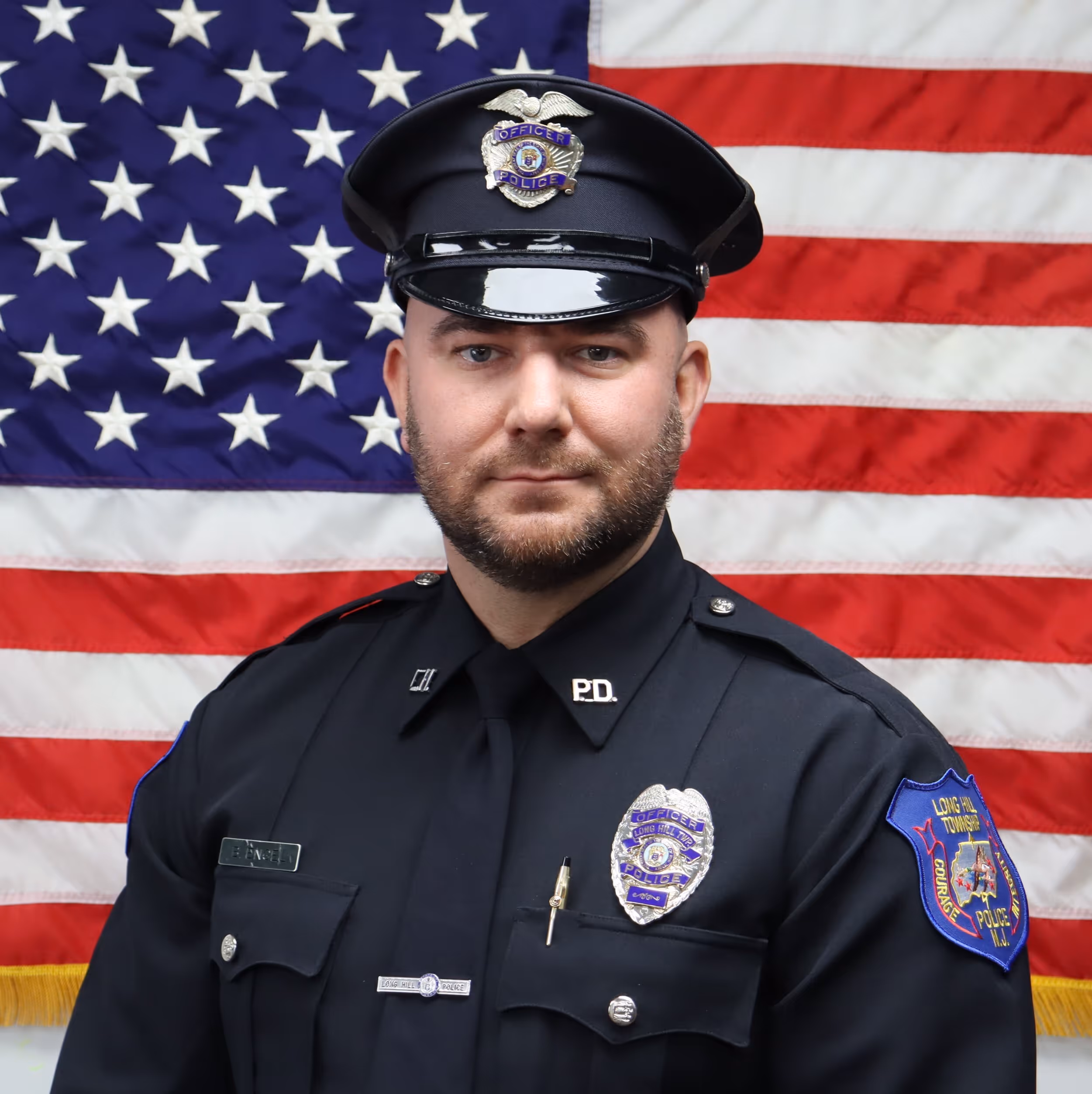 Portrait of a male police officer in uniform standing in front of an American flag.