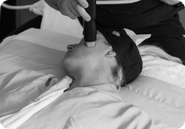 Person lying down with eyes covered receiving a facial treatment using a handheld device.