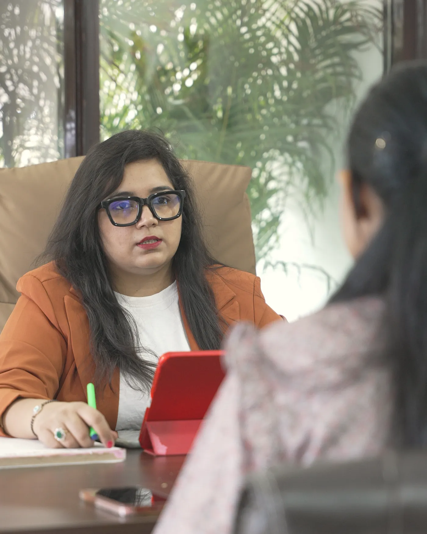 A consultation at VinayakM: a member of the team listens closely and takes notes while a visitor, seen from behind, talks across the desk.