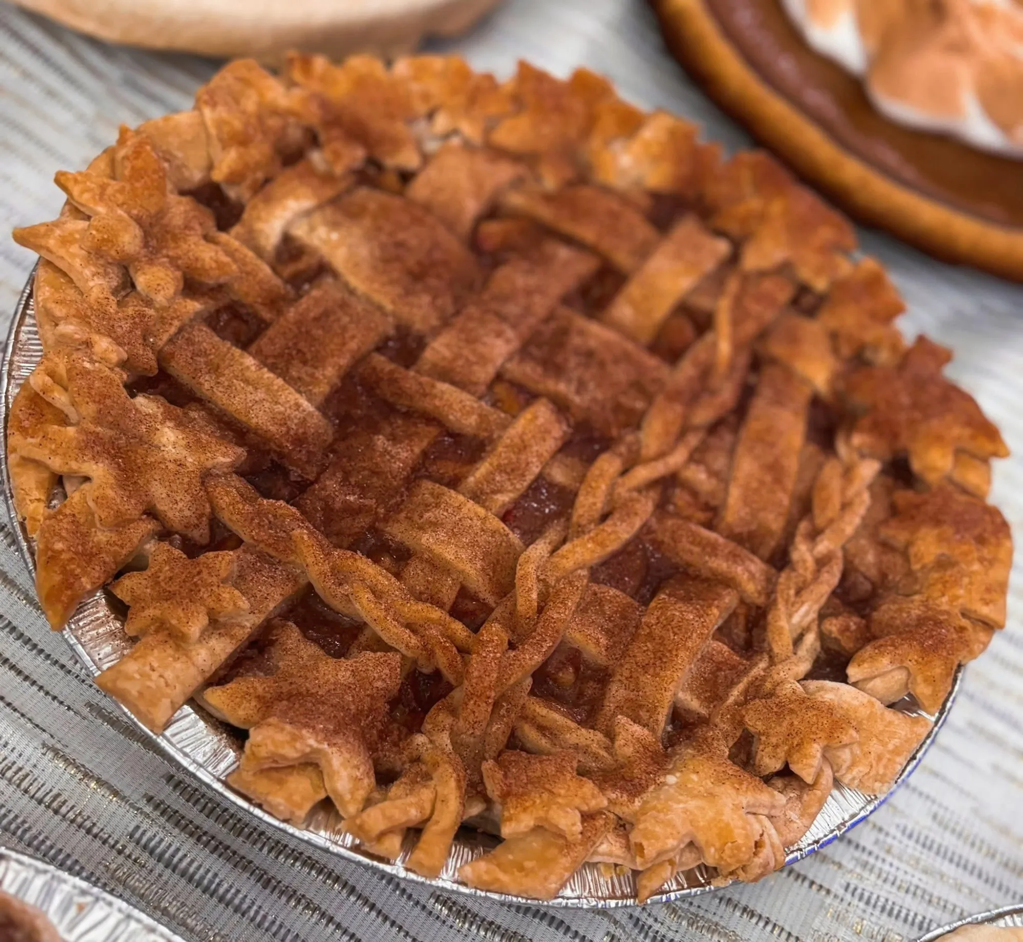 Close-up of a homemade lattice-top apple pie with braided crust edges and leaf-shaped pastry decorations.