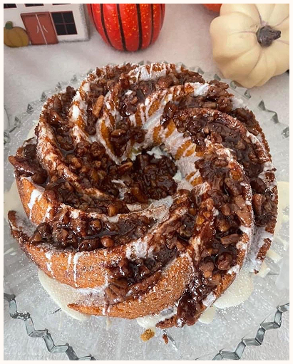 Bundt cake with chocolate drizzle and chopped nuts on a glass plate, with pumpkins and fall decorations in the background.