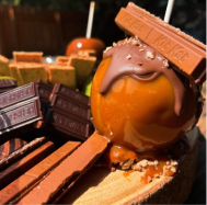 Caramel ball topped with melted milk chocolate and KitKat pieces on a wooden surface.