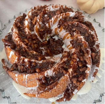 Swirled bundt cake topped with powdered sugar and chopped nuts drizzled with chocolate sauce on a glass plate.