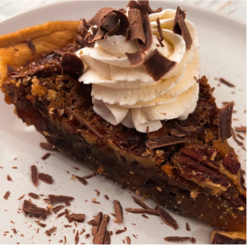 Slice of pecan pie topped with whipped cream and chocolate shavings on a white plate.