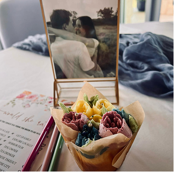 Small bouquet of colorful artificial flowers wrapped in paper with a framed black and white photo of a couple embracing in the background.