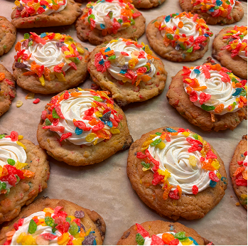 Cookies topped with white frosting swirled in the center and sprinkled with colorful cereal pieces.