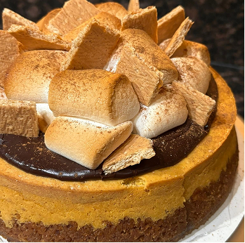 Close-up of a cheesecake topped with chocolate ganache, toasted marshmallows, and broken graham crackers.