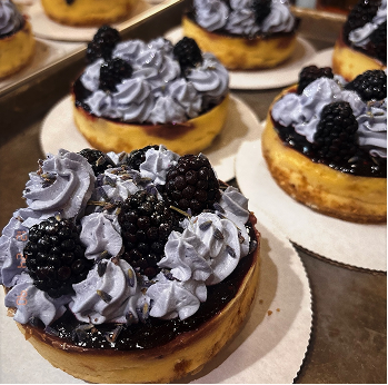 Individual blackberry cheesecakes topped with whipped cream and fresh blackberries on white paper doilies.