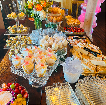 Elegant buffet table with assorted finger foods, desserts, and flower arrangements on glass serving platters.