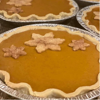 Close-up of pumpkin pies in aluminum pans, decorated with leaf-shaped pastry cutouts on top.