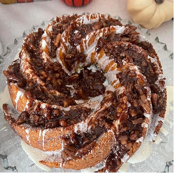 Bundt cake topped with powdered sugar, chopped nuts, and drizzled chocolate on a glass plate.