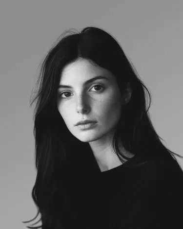 Portrait en noir et blanc d'une femme aux longs cheveux noirs, regardant directement l'appareil photo avec une expression neutre.