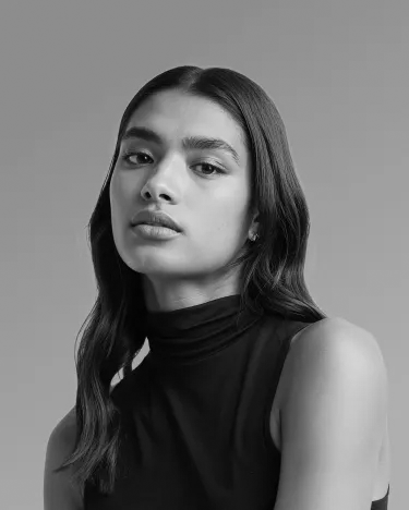 Portrait en noir et blanc d'une femme avec les cheveux longs ondulés portant un haut noir sans manches à col roulé.