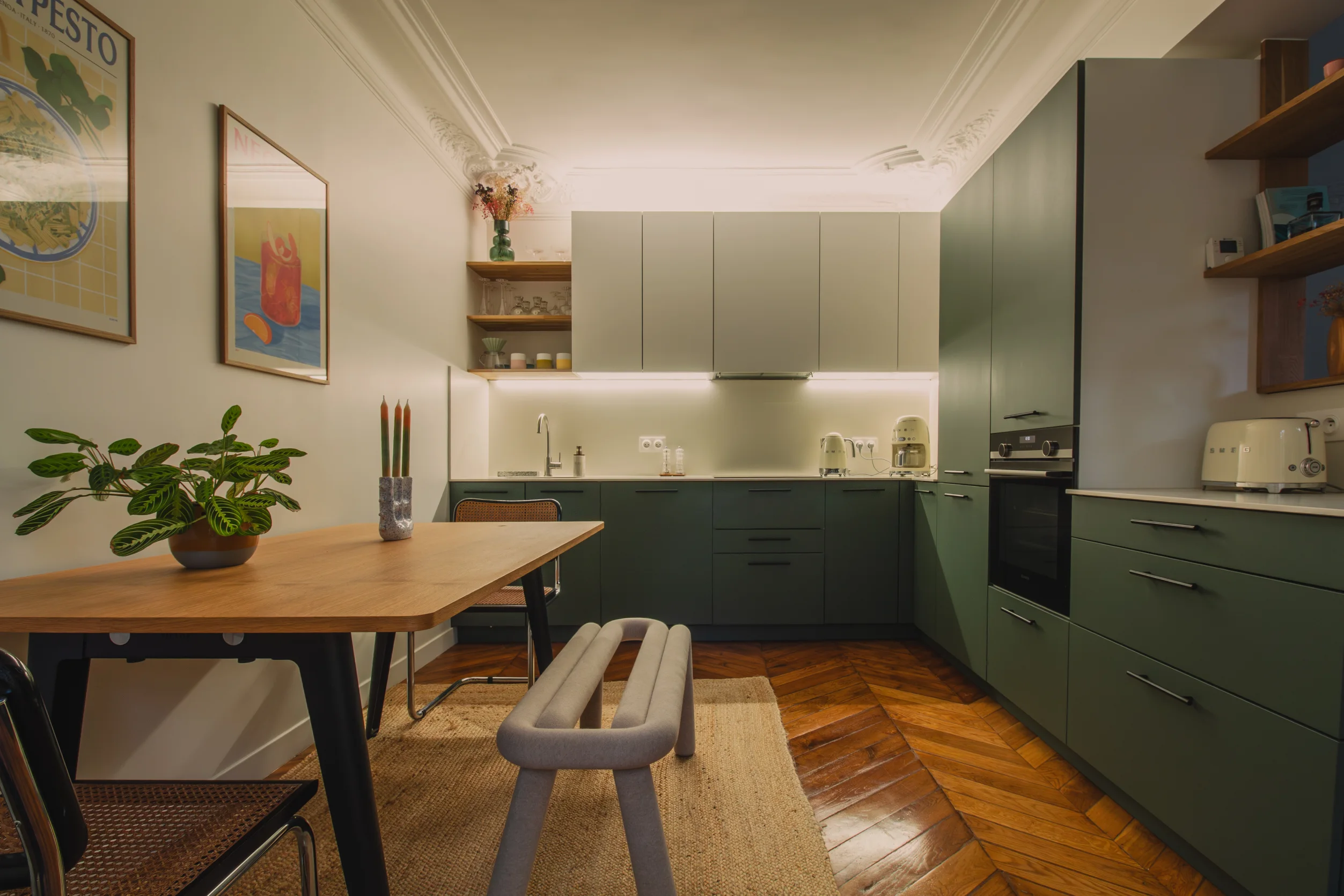 Cuisine moderne avec des armoires basses vertes, des armoires hautes blanches, un parquet en bois et une table à manger avec une plante et des bougies.