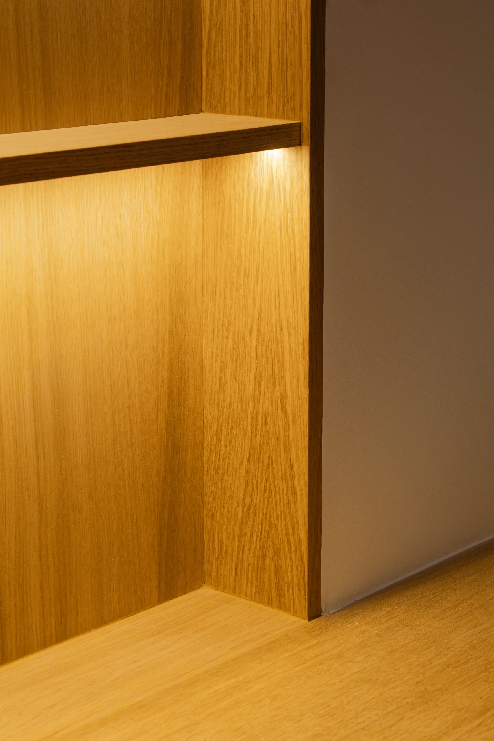 Coin d'une étagère en bois avec éclairage LED intégré et texture bois brun clair.