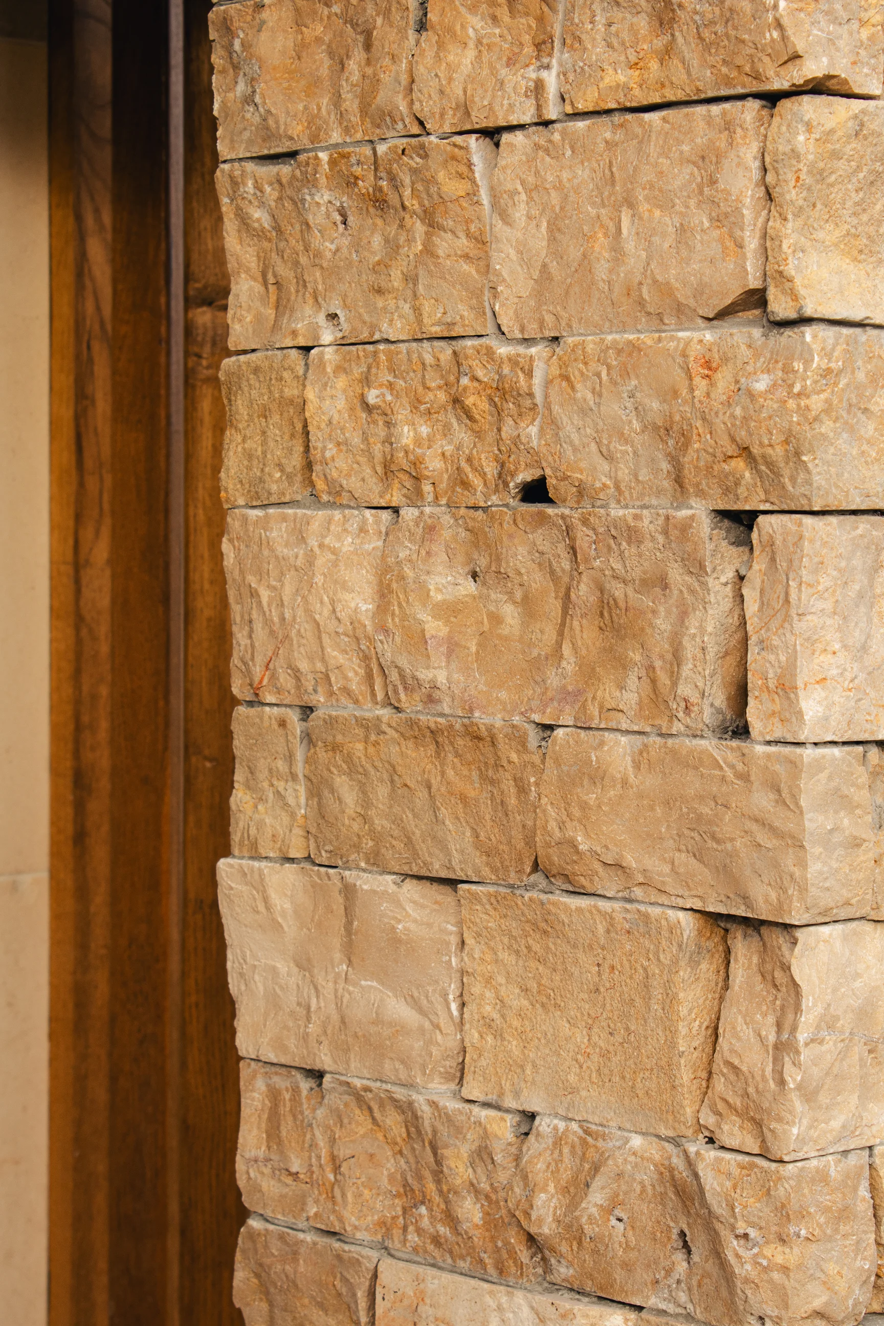 Gros plan d'un mur en pierres beiges avec des pierres rectangulaires grossièrement taillées à côté d'un encadrement de porte en bois.