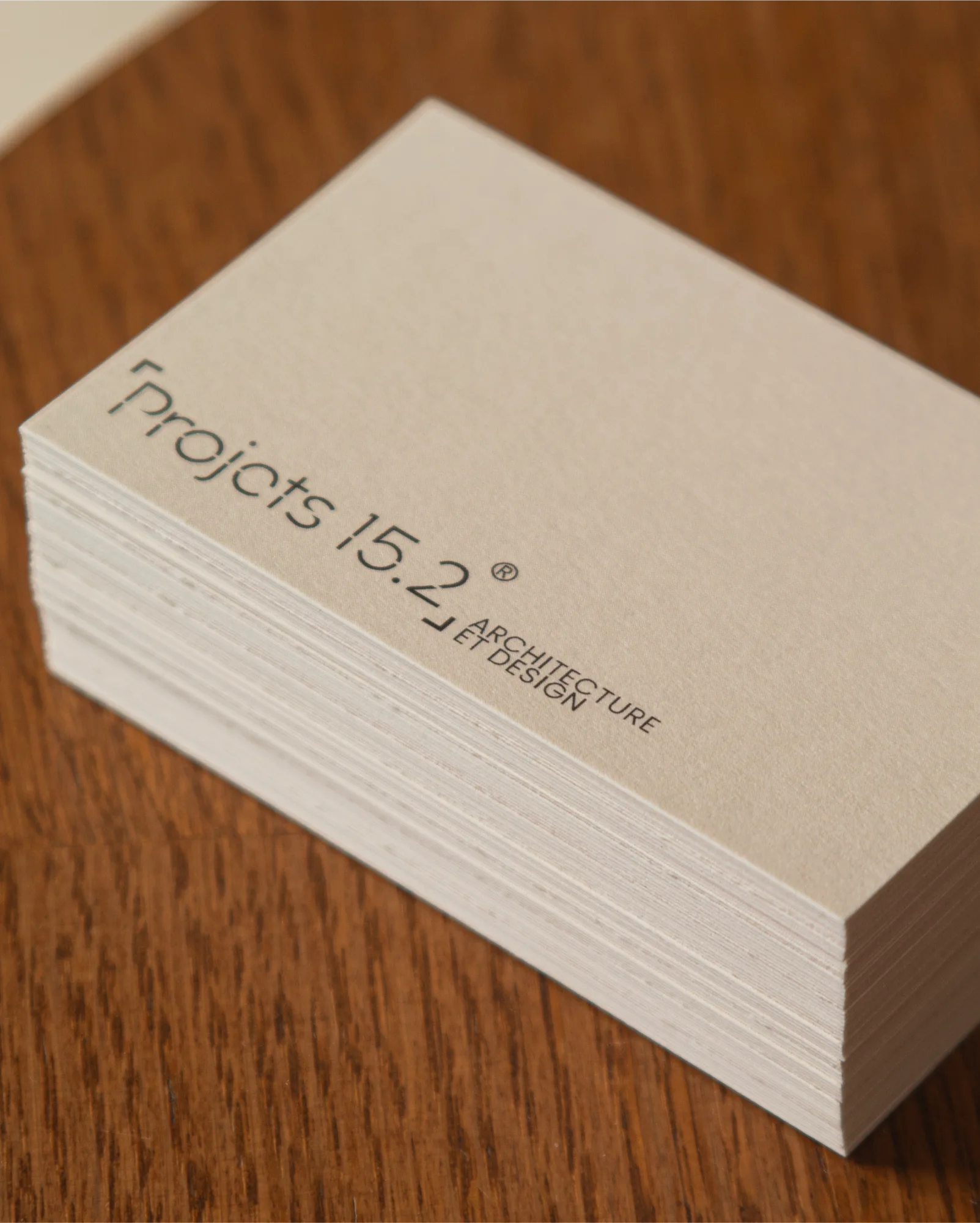 Pile de cartes de visite beiges sur une surface en bois avec l'inscription « Projects 15.2 Architecture Et Design » imprimée en noir.