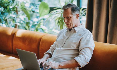 Ein Mann in einem hellen Hemd, der auf einem orangenen Sofa sitzt.