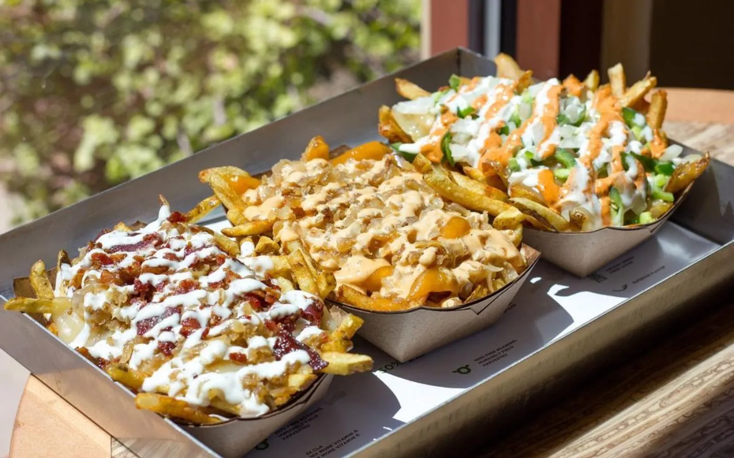 Three trays of loaded fries are placed in a metal serving dish.