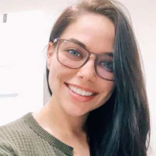 Smiling woman with long dark hair, wearing oversized eyeglasses and a green knit sweater.