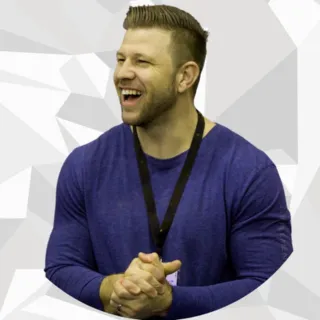 Smiling man with clasped hands wearing a blue sweater and black lanyard against a geometric gray background.