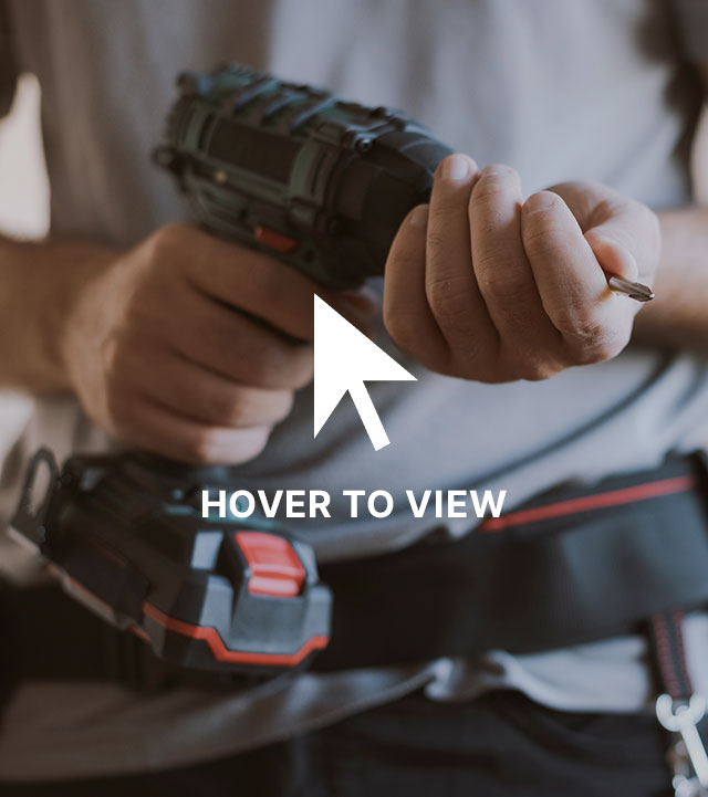 Person holding a cordless power drill with a screwdriver bit, wearing a gray shirt and a tool belt.