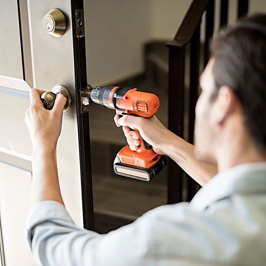 Person using an orange cordless drill to install or fix a door lock.