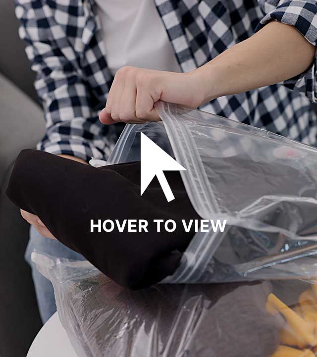 Person wearing a checkered shirt packing or unpacking a black folded garment into a clear plastic storage bag.